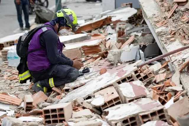 Un rescatista con casco, tapabocas y chaleco morado usa un dispositivo de detección de sonido sobre los escombros de un edificio en Catia La Mar, Venezuela.