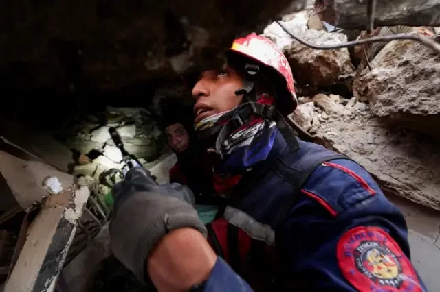 Un bombero, que lleva casco y un abrigo resistente, sostiene una pequeña cámara de búsqueda en la mano mientras busca sobrevivientes del terremoto.