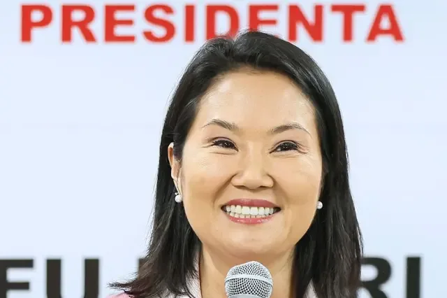 Keiko Fujimori sujeta sonriente un micrófono. Tras ella hay un cartel con el mensaje "Presidenta Fujimori".