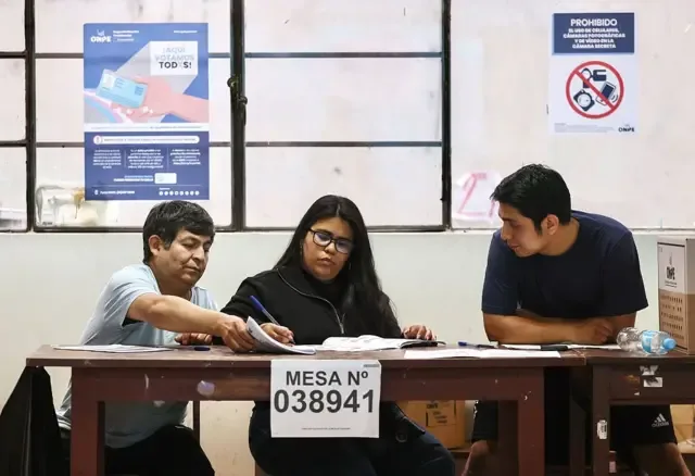 Tres personas tras una mesa electoral en un centro de votación de Lima.